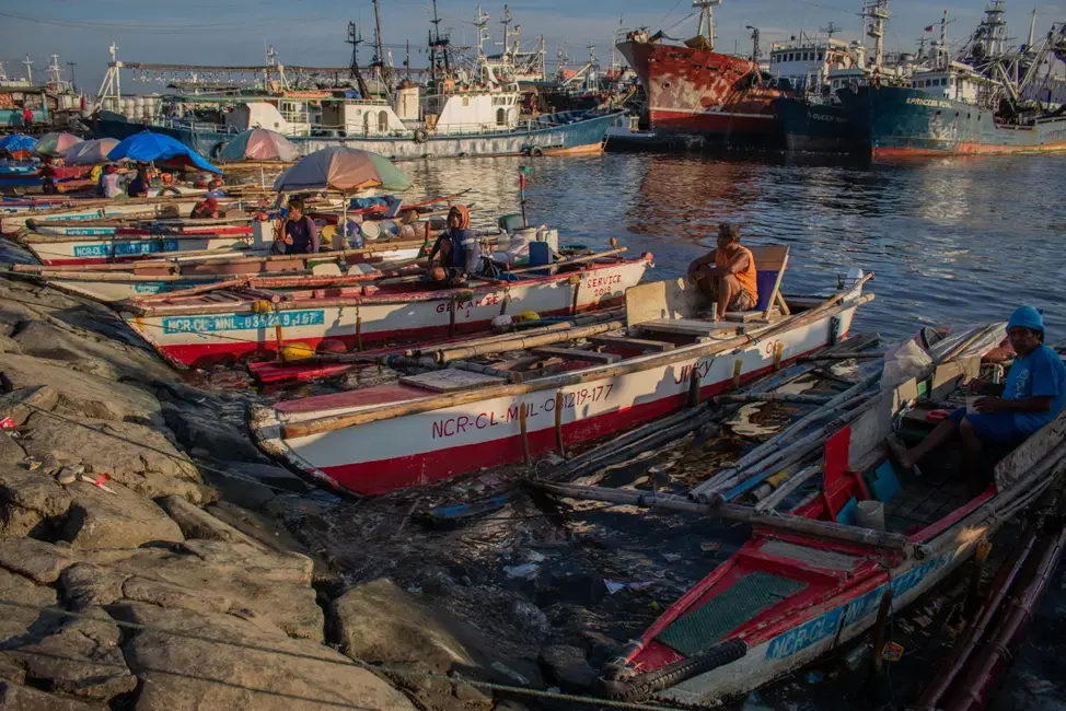 A few men sitting on their boats, waiting for passengers on a Wednesday afternoon at the Navotas Fish Port Complex. Their passengers are typically men who work in cargo ships and fishing boats in Manila Bay. Image by Micah Castelo. Philippines, 2019.