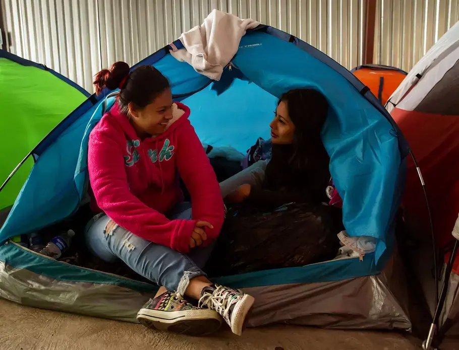 Gabriela, 22, left, and friend Daniela, 19, talk in a shelter in Tijuana. Gabriela, mother of two children, was shot several times in El Salvador. They talked about the risks women can face in their home country, including sexual assault, violence and death. The women fled and were in the process of applying for asylum. Image by Erika Schultz. Mexico, 2019.