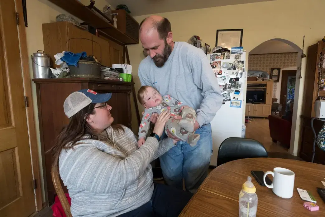 Carrie and Patrick Mess hand off their 10-month-old son, Ben, on the family's farm in Watertown. They hope to give their two sons the choice of becoming the next generation of family farmers when they become adults. Image by Mark Hoffman. United States, 2019.