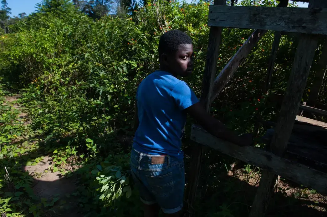 A sliver of sun illuminates the eye of 11-year-old Adipi Revanildo as he stands the farmlands that run behind his family's shacks off of Suriname's Afobaka Road. His father, Nelson Adose Martines, teaches him math with a blackboard. Image by Stephanie Strasburg. Suriname, 2017.
