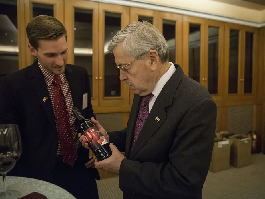 Aaron Hermsen, director of business development for the China Iowa Group gives a bottle of Jasper Winery wine to Terry Branstad, U.S. ambassador to China, during an Iowa Sister States reception on Wednesday, Sept. 20, 2017, in Beijing, China. The wine, with a special Iowa, China label is the same kind that was severed during the state dinner held when China's president Xi Jinping visited Iowa in 2012. Image by Kelsey Kremer. China, 2017.
