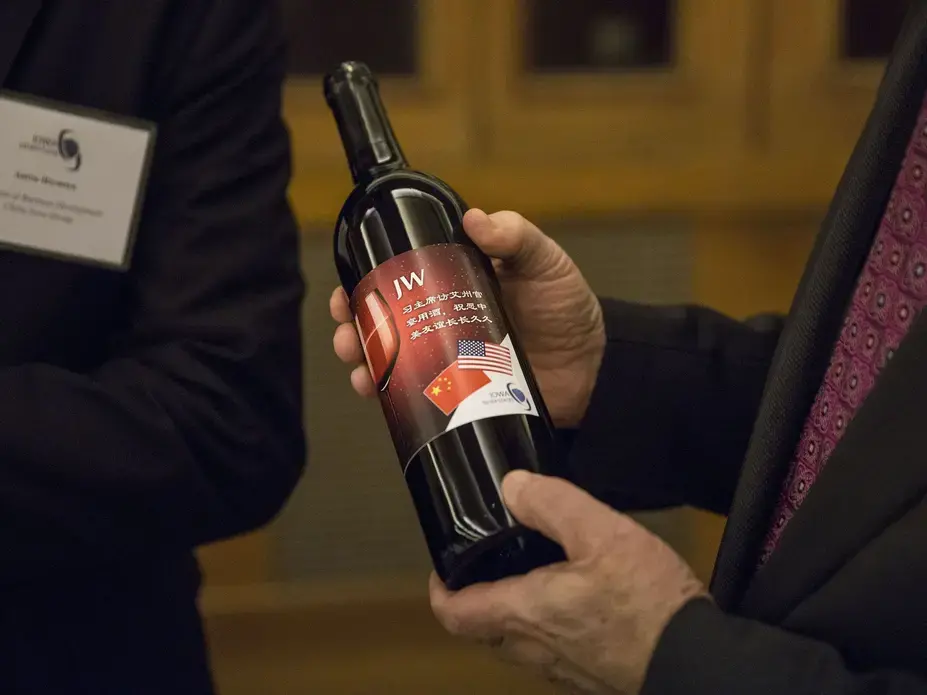Aaron Hermsen, director of business development for the China Iowa Group gives a bottle of Jasper Winery wine to Terry Branstad, U.S. ambassador to China, during an Iowa Sister States reception on Wednesday, Sept. 20, 2017, in Beijing, China. The wine, with a special Iowa, China label is the same kind that was severed during the state dinner held when China's president Xi Jinping visited Iowa in 2012. Image by Kelsey Kremer. China, 2017.<br />
