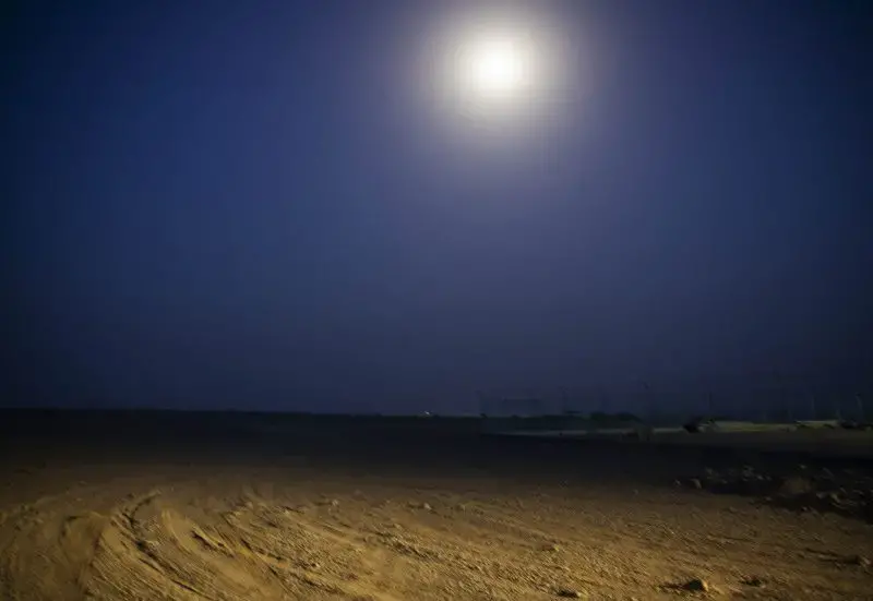 The moon shines on the beach, July 14, 2019, in Obock, Djibouti, where smugglers take Ethiopian migrants by boat to Yemen. The trek through Djibouti ends on a long, virtually uninhabited coast outside the town of Obock, the shore closest to Yemen. Here migrants would stay, sometimes for several days, and wait for their turn on the boats that every night cross the narrow Bab el-Mandeb strait to Yemen. Image by AP Photo / Nariman El-Mofty. Djibouti, 2019.