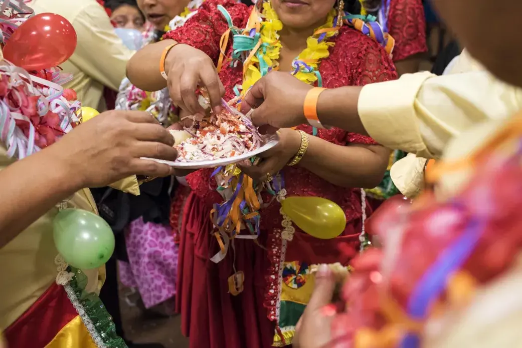 A group of friends share a traditional q’allu salad of tomato, onion, and cheese. These friends are part of a music and dance group, which are called comparsas, and they go by “Los Renegados” or “The Renegades.” At every carnival party, each comparsa presents their prepared dance and perform Quechua/Spanish couplets for the couplet competition. People in each group match their clothing and celebrate the night together.  Image by Carey Averbook. United States, 2016.