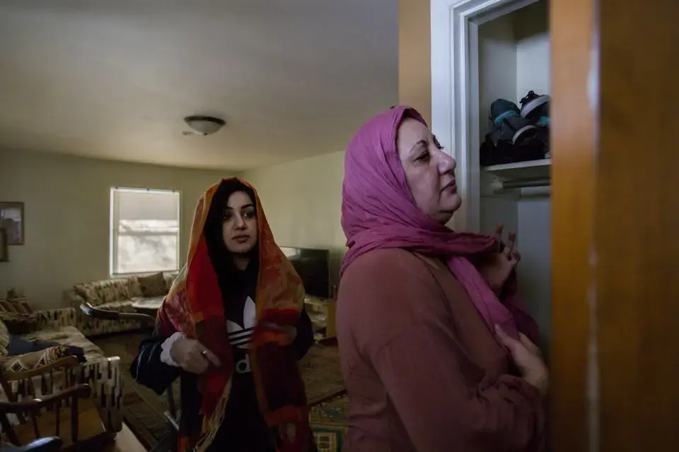 Zahra Ahmad, 24, watches as her mother, Lamiya Adil Mahdi, demonstrates how to wrap a hijab in her home in Lansing, Michigan on Friday, Feb. 1, 2019, hours before she departs for Iraq. Image by Brontë Wittpenn. United States, 2019.