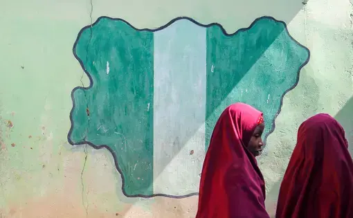 MAIDUGURI, NIGERIA - September 9, 2015: Girl students pass a classroom with the map and flag of Nigeria painted on it, at Success Private School, one of the first schools attacked by Boko Haram in '09. Image by bmszealand/Shutterstock.