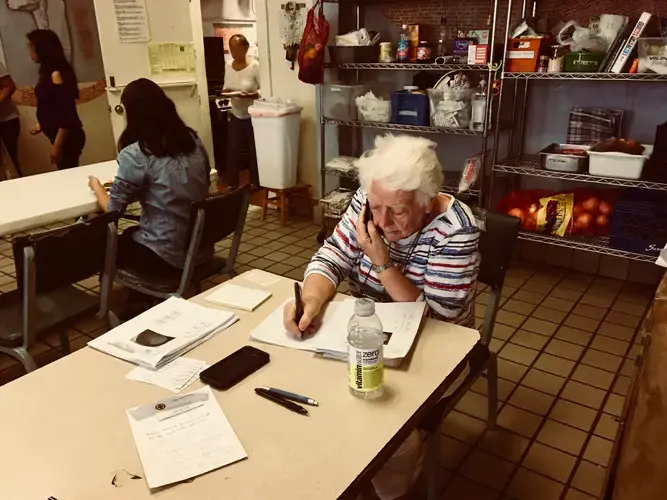 Sister Caroline Sweeney, a volunteer, calls relatives of the new arrivals to help them make travel plans. Most migrants leave Casa Vides after one night to join family or friends living elsewhere in the U.S. Image by Lily Moore-Eissenberg. United States, 2019.