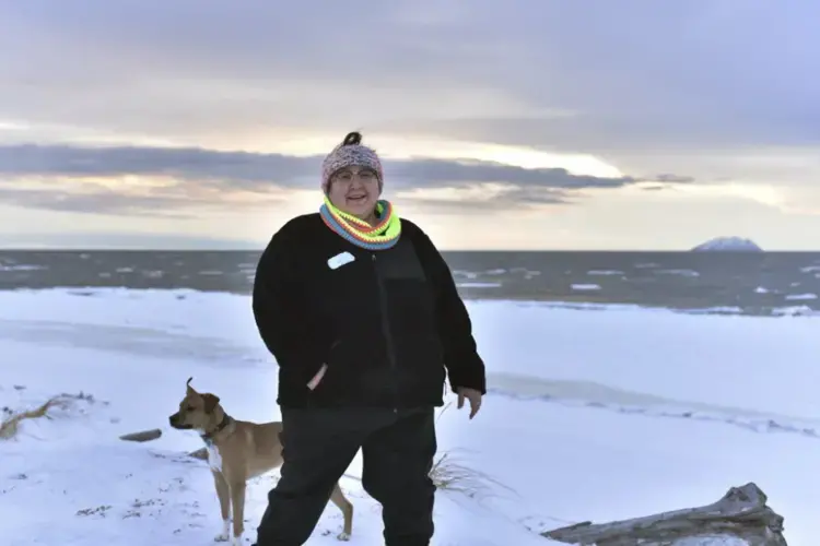 In this Jan. 14, 2019 photo, Clarice 'Bun' Hardy stands on the beach with her dog, Marley, in the Native Village of Shaktoolik, Alaska. Hardy, a former 911 dispatcher for the Nome Police Department, says she moved back to her village after a sexual assault left her feeling unsafe in Nome. Image by Wong Maye-E. United States, 2019.