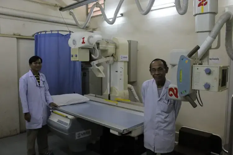 In Sihanouk Hospital Center of HOPE, in Phnom Penh, radiologists pose with one of the hospital's two donated X-ray machines.  The hospital is an international charity with a creative operating model: the hospital receives international donations of medicine and equipment, and only charges patients for care that draws on resources that the hospital had to purchase; if diagnosis or treatment is undertaken with donated resources, then the patient isn’t charged. Image by M. G. Zimeta. Cambodia, 2018.