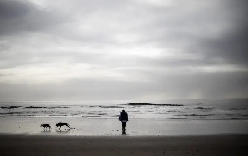 Carmall Casey walks with her dogs on the beach in Hellyer, Tasmania, Australia, Wednesday, July 24, 2019. 'It's like freedom when I'm on the beach,' said Casey. 'I look at the footprints and different shells and it helps to release all my stress and worries.' Image by David Goldman. Australia, 2019.