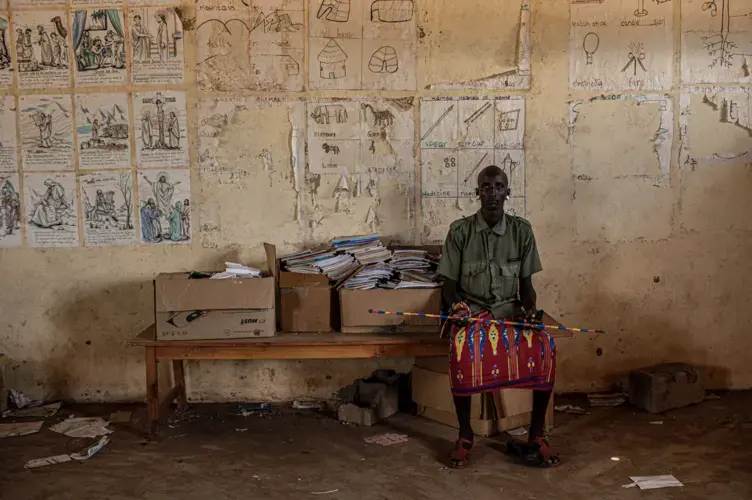 A young Rendille moran sits in a shuttered school building near the town of Laisamis in Kenya. Young men broke the windows of the school and have been living in the classrooms since the school was closed due to the COVID-19 pandemic. Image by Will Swanson. Kenya, 2020.