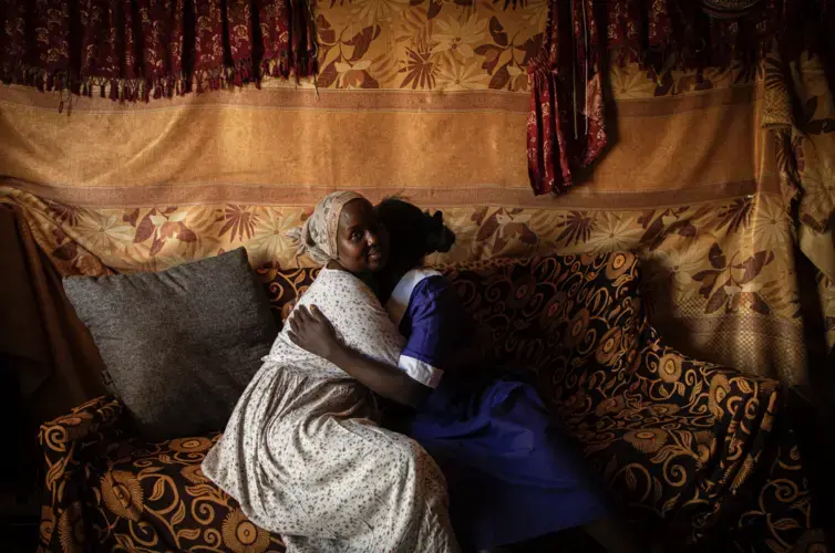 Dorcas Choya sits with Susie on her couch, who fled her home when her parents brought a circumciser to cut her. “When I saw her I just ran,” said Susie. “I didn’t bother taking anything. I ran without shoes.' Image by Will Swanson. Kenya, 2020.