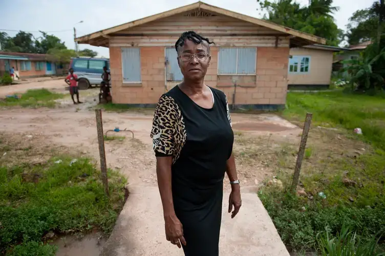 Gladys Renfurm, an elementary school teacher, stands above pooled water tainted with sewage in her neighborhood in Moengo, Suriname. “If it has rained, you can’t breathe.' Image by Stephanie Strasburg. Suriname 2017.