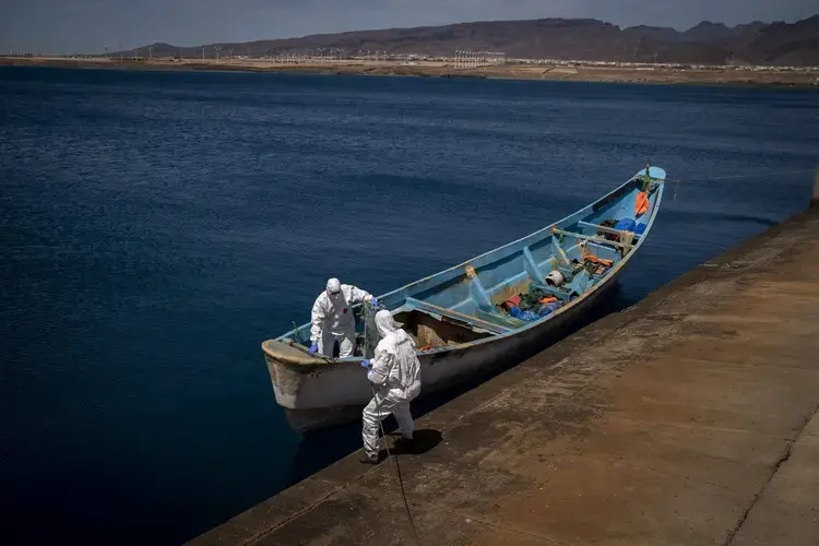 Police officers inspect a boat where 15 Malians were found dead adrift in the Atlantic on Thursday, Aug. 20, 2020, in Gran Canaria island, Spain. Image by Emilio Morenatti/AP Photo. Spain, 2020.