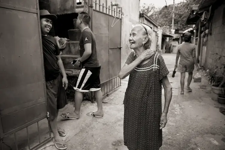 Narcisa Claveria laughs with neighbors in this 2019 photo. Even in the coronavirus pandemic, she goes out, wearing a mask. 'I'd rather die in the streets,' she says, 'than stay dying of sadness at home.' Image by Cheryl Diaz Meyer. Philippines, 2019.