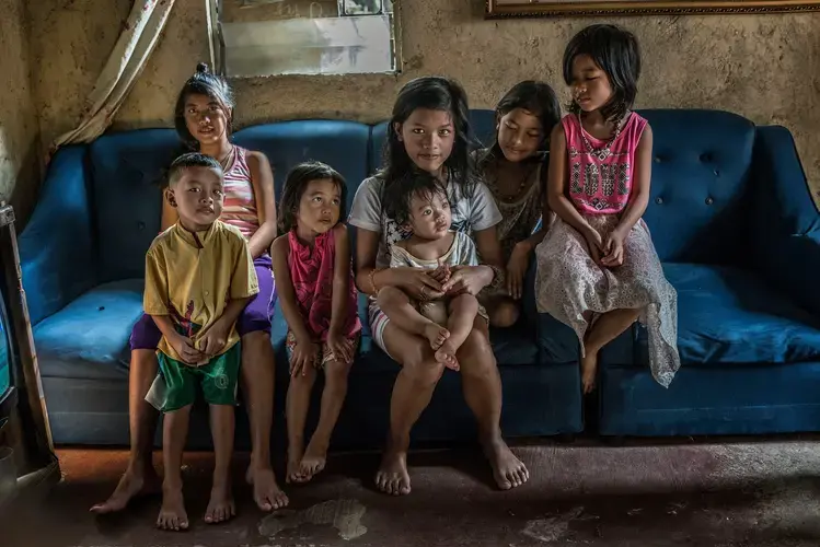 Constantino de Juan’s seven children sit on a sofa that still bears the bullet hole from their father’s shooting. Juan was preparing a spaghetti dinner on his daughter’s birthday when he was killed. Image by James Whitlow Delano. Philippines, 2017.