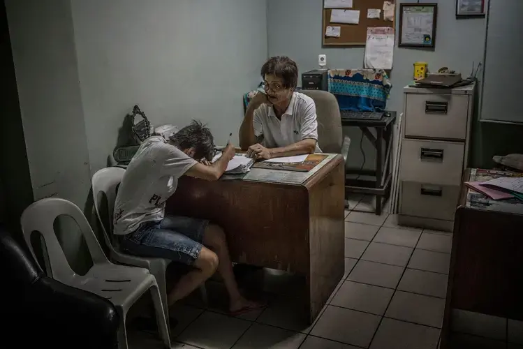 Ginnalyn Soriano breaks down in tears in front of Orly Fernandez, operations manager at Eusebio funeral home, as she fills out the required paperwork following the death of her brother Julius. Image by James Whitlow Delano. Philippines, 2017.