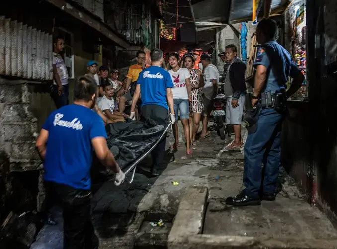 Ginnalyn Soriano, 21, looks on as the body of her elder brother, 24-year-old Julius, is carried away following his execution. His body showed signs that his hands had been bound before he was shot during a police operation in Caloocan, in the Metro Manila area, as part of the war on drugs. Image by James Whitlow Delano. Philippines, 2017.