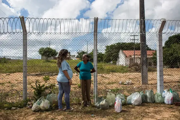 Two women gather near the prison. They are surrounded by plastic bags filled with food. Image by Lianne Milton. Brazil, 2018.
