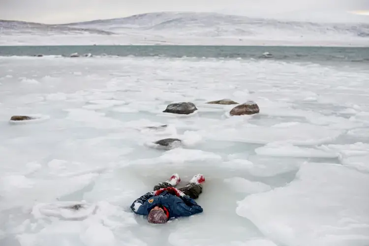 Waiting for help during a search-and-rescue training exercise, a Canadian Ranger lies in a pool of melted ice near the Clyde River community on Baffin Island. The Rangers are a volunteer reserve group mostly from Native communities across northern and remote regions in Canada. Image by Louie Palu. Canada, 2018.