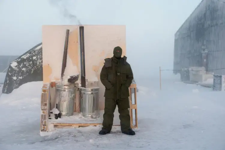 Canadian army Corporal Stewart Hickman keeps watch over two immersion heaters—devices used to melt snow and ice to make water—at an Arctic training camp in Hall Beach, Nunavut. Crucial for survival, water can be difficult to obtain during winter military operations, and large amounts of fuel are necessary to continuously melt snow and ice. Image by Louie Palu. Canada, 2018.