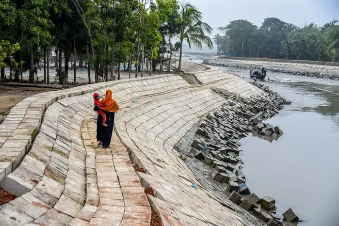 A woman walks by a canal linking the Kobadak River to a polder. Connecting the canal and the river causes flooding in one place that might protect land elsewhere. Image by Tanmoy Bhaduri. Bangladesh, 2017.