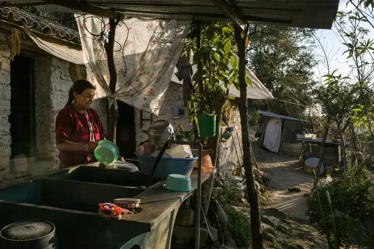 Clara Luz Lucas washes dishes outside her home, in the western highlands. Lucas has a daughter living in Houston. Image by Mauricio Lima. Guatemala, 2019.