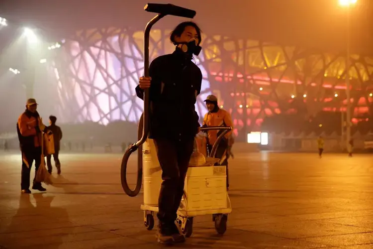 'Brother Nut' collects smog with an industrial vacuum cleaner near the Bird's Nest stadium in Beijing, in November 2015. He later made the dust into a brick. Image by Dong Dalu, VCG. China, 2015.