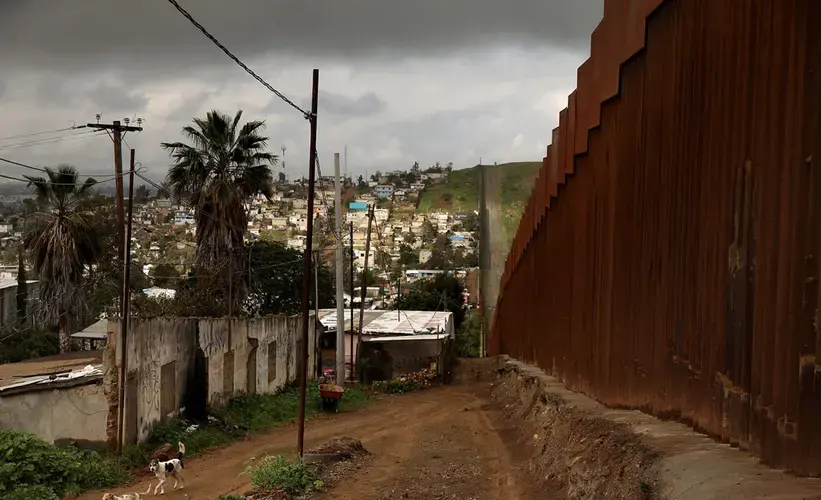 Dogs walk by the U.S.-Mexico border fence in the East Tijuana neighborhood of El Nido de las Aguilas, or The Eagle’s Nest. Image by Erika Schultz. Mexico, 2019.