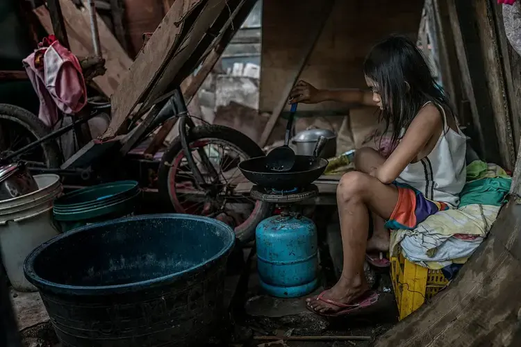 Lenie Banting’s other daughter, Rubylyn prepare an egg over a propane flame at their makeshift house on the former Smoky Mountain dumpsite. Image by James Whitlow Delano. Philippines, 2018. 