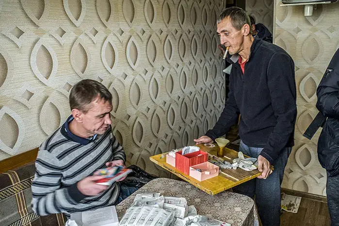 Vyacheslav Ignatenko (right), holding a tray of opiate cooking equipment, receives bags of syringes from a needle exchange in Kazan, Russia. Image by Misha Friedman. Russia, 2018.