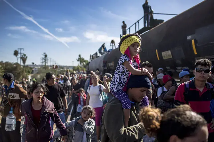 Hundreds of Hondurans move towards the border wall, coasting the wagons of the trains parked near the vehicle port of Chaparral. Image by Simone Dalmasso. Tijuana, 2018.