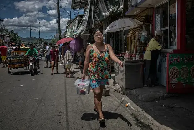 Rhoda, a widow who is raising seven children after her husband was killed in an extrajudicial killing, walks through the streets of Payatas to deliver an Avon product, which she started selling door to door in January 2018. Image by James Whitlow Delano. Philippines, 2018. 