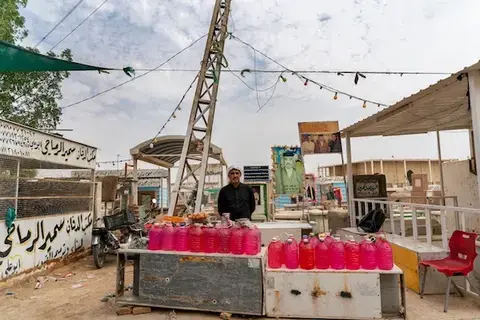 A man stands behind a table where he has jugs of red liquid for sale