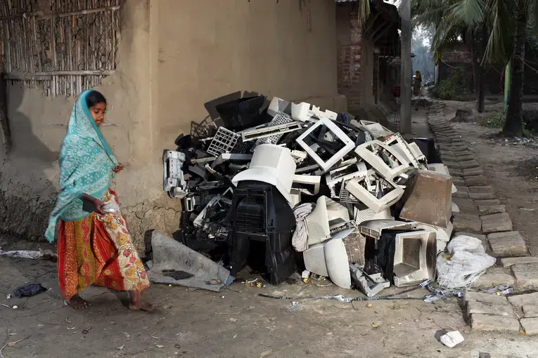 A girl walks past the shells of computer monitors that have been stripped of valuable wire and metals, but which can still bring a small payment from a plastics recycler. Many residents in her village, Sangrampur, are involved in the e-waste trade. Image by Sean Gallagher. India, 2014.