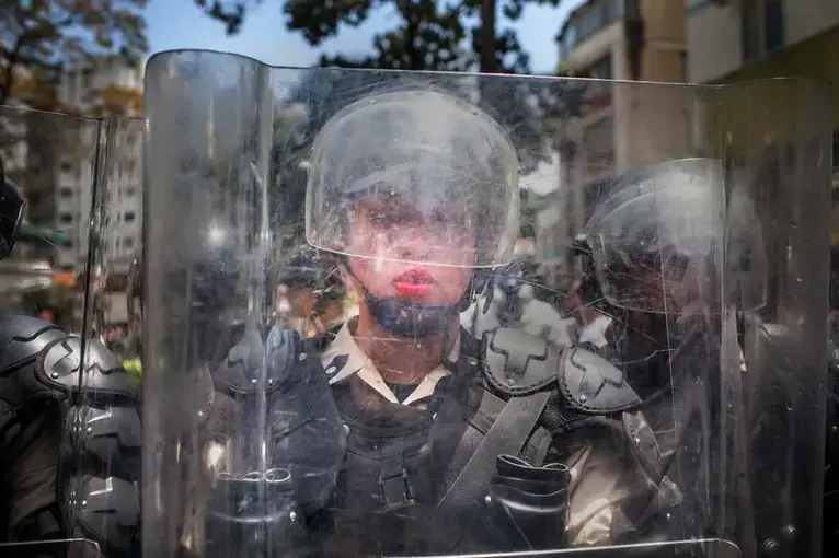 A National Police officer behind a riot shield is pushed backward by a crush of demonstrators during the March of the Empty Pots in Caracas in 2014, which coincided with International Women's Day. Image by Natalie Keyssar. Venezuela, 2014.