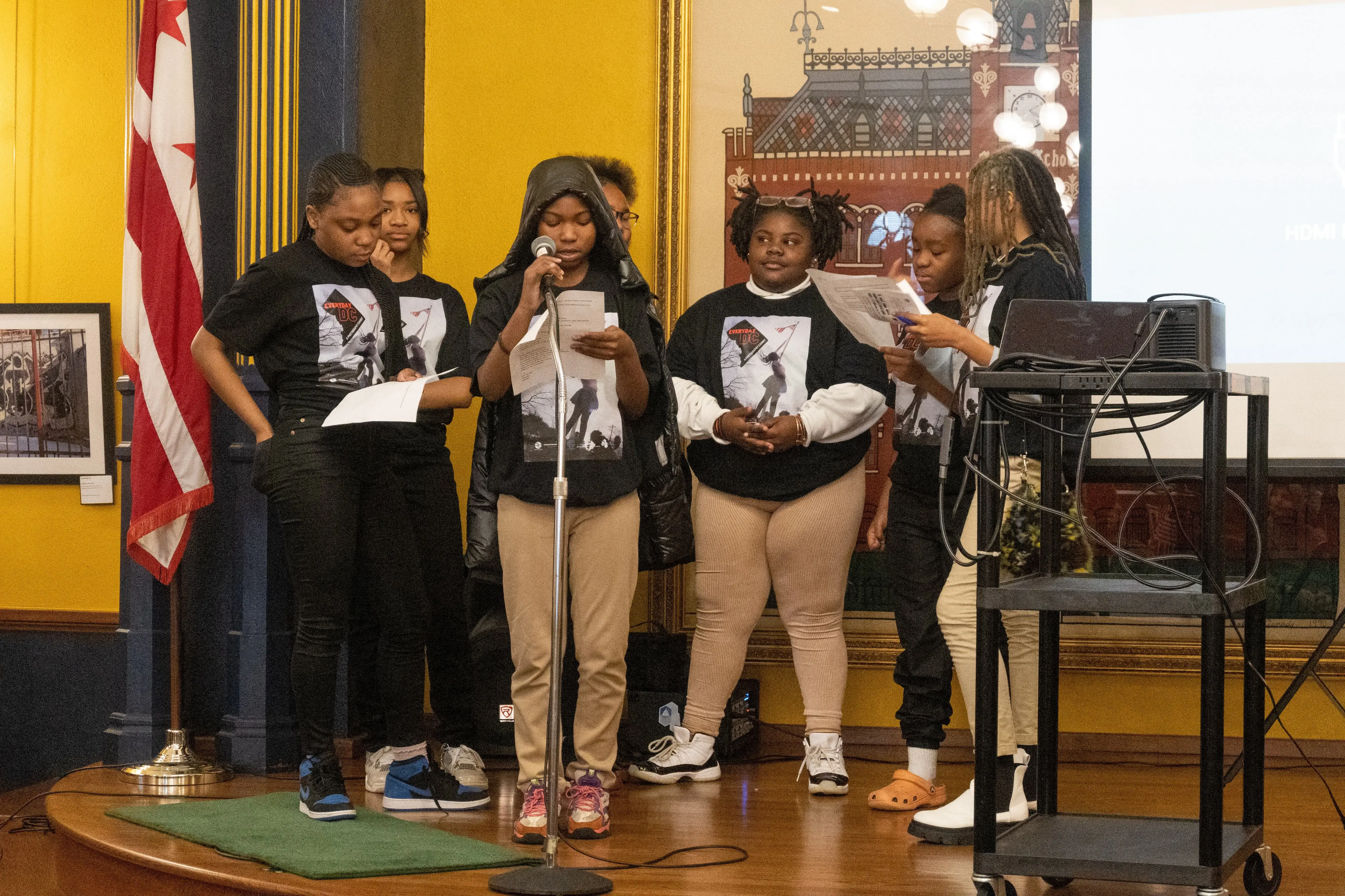 nine students wearing black shirts with the logo for Everyday DC stand on stage at the Charles Sumner Museum to present their curator remarks