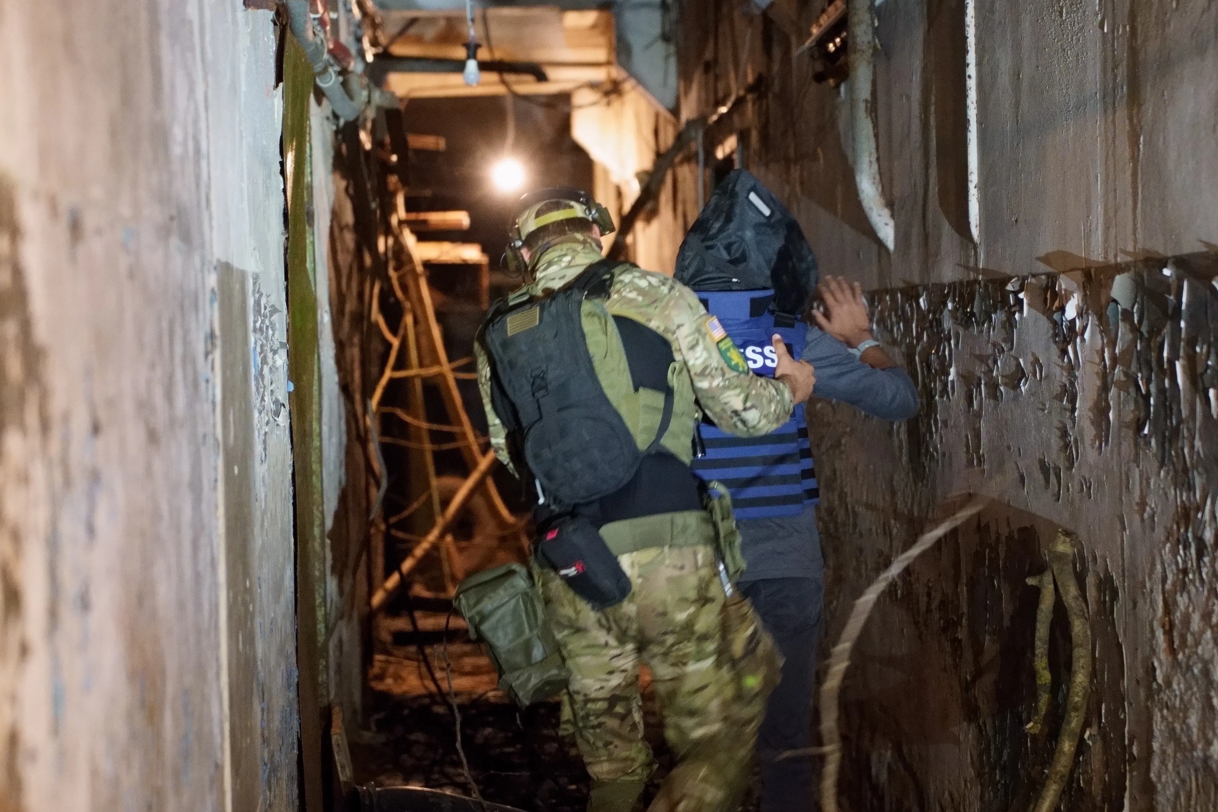 A man in military gear leads another guy down the tunnel