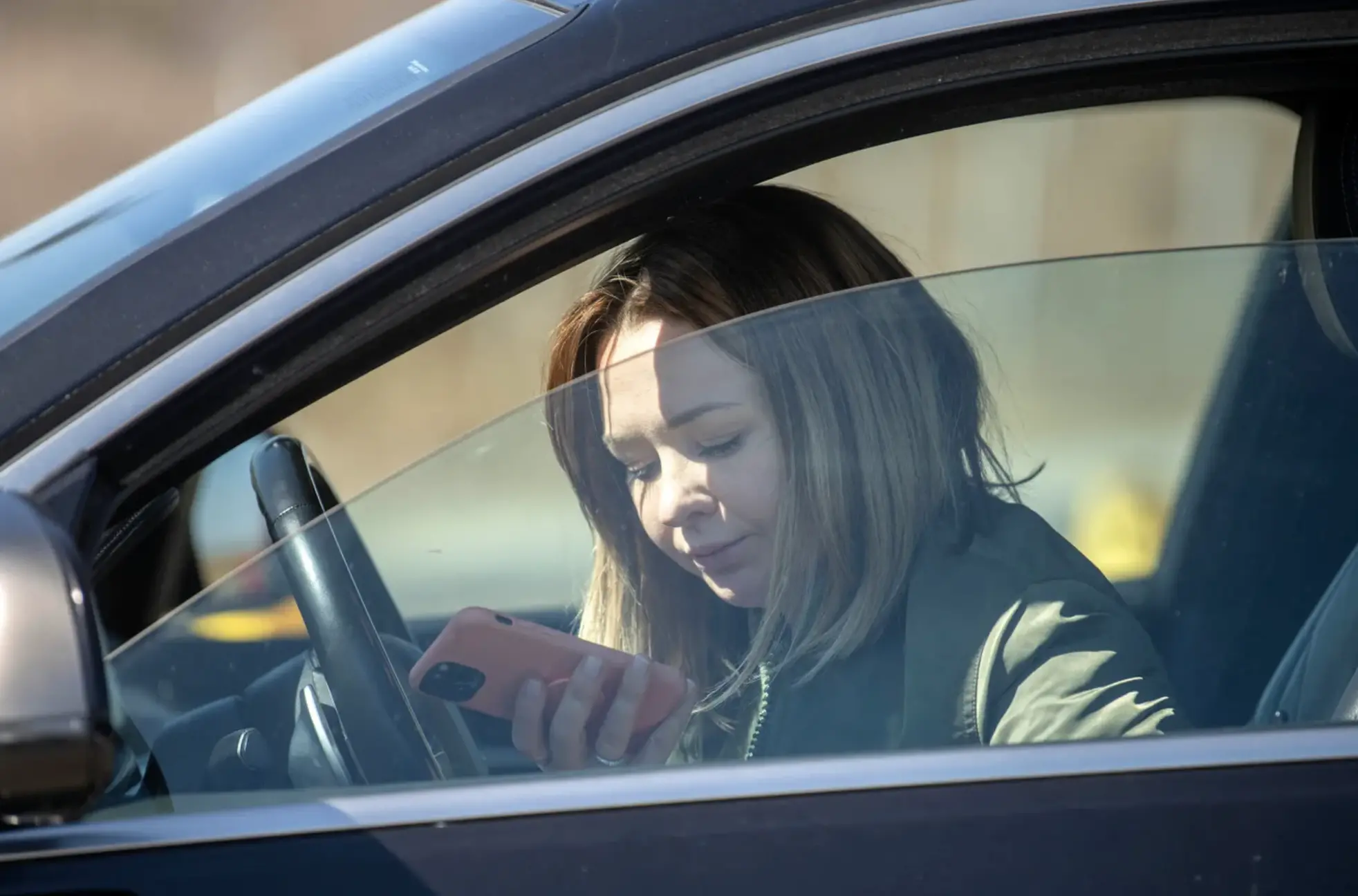 A girl sits in her car looking at her phone