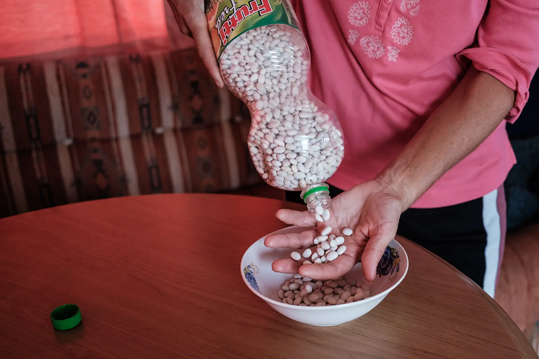 Paula pours dried beans from a recycled plastic soda bottle into a bowl