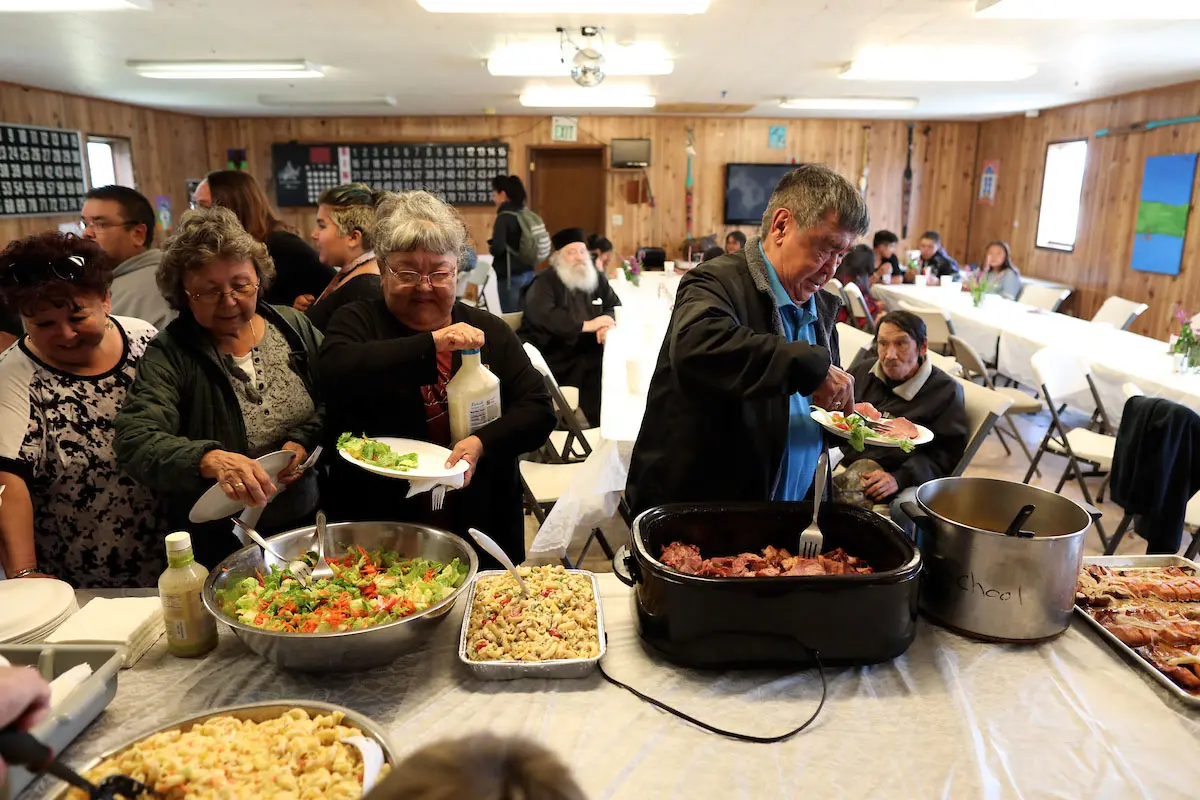 Men and women serve themselves at a potluck-style dinner.