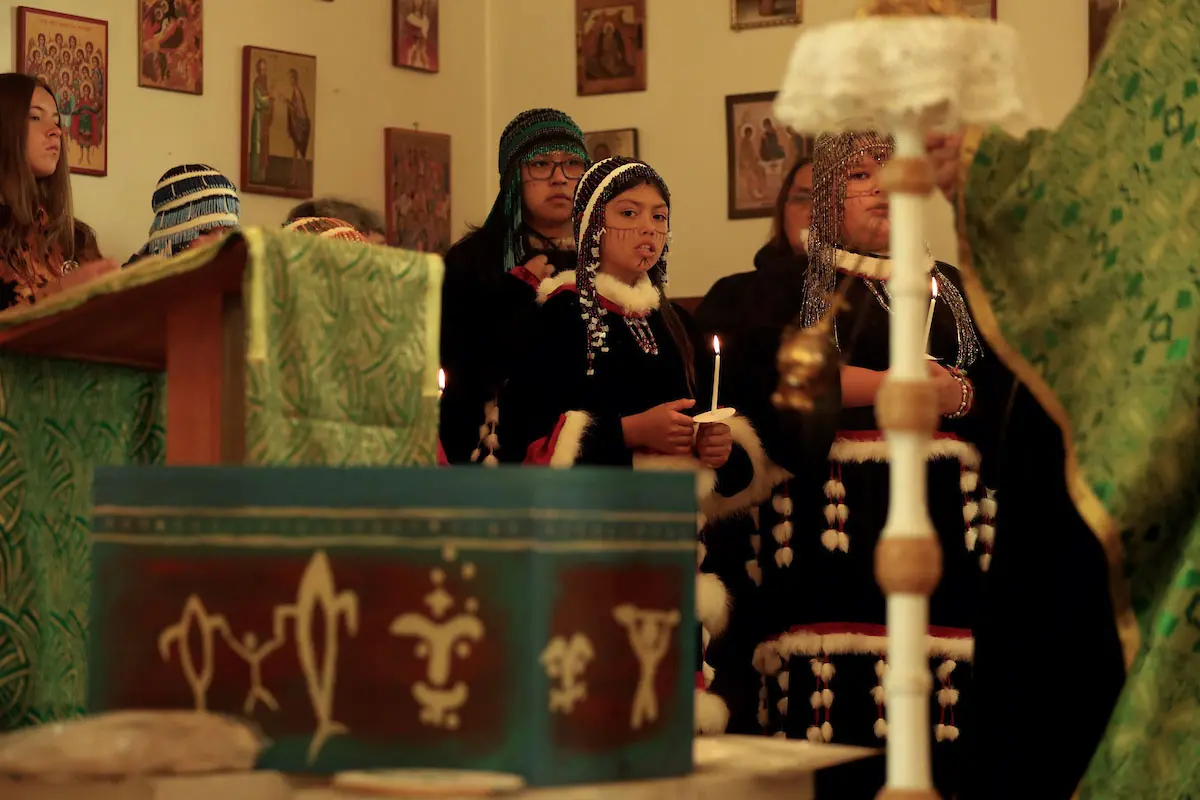 Women and girls in beaded headdresses and regalia hold lit candles before the box of Anastasia's remains.