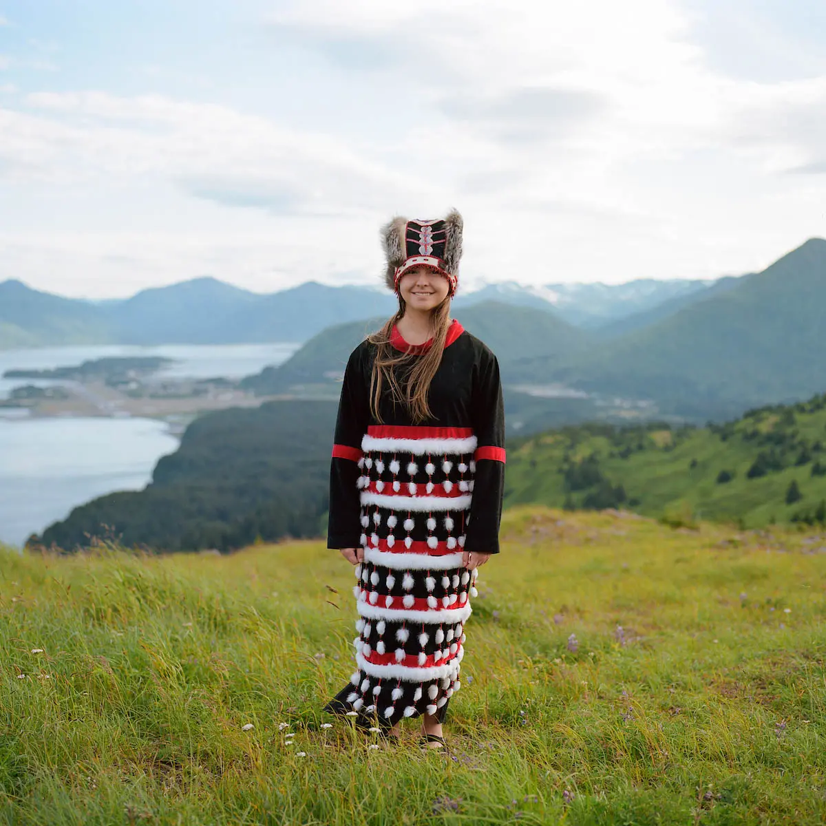 A girl in regalia standing before a mountainscape.