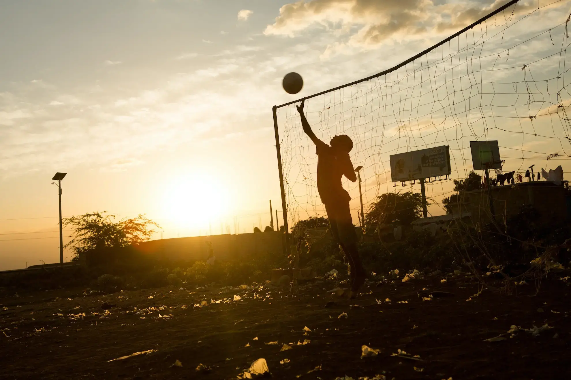 sillouette of a kid reaching for a ball in front of a net at sunset