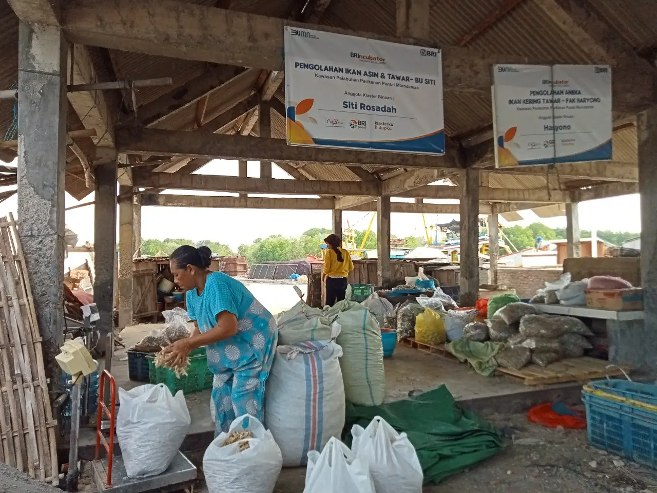 A fisherwoman weighs dried fish at the dried and salted fish center surrounded by other bagged food items