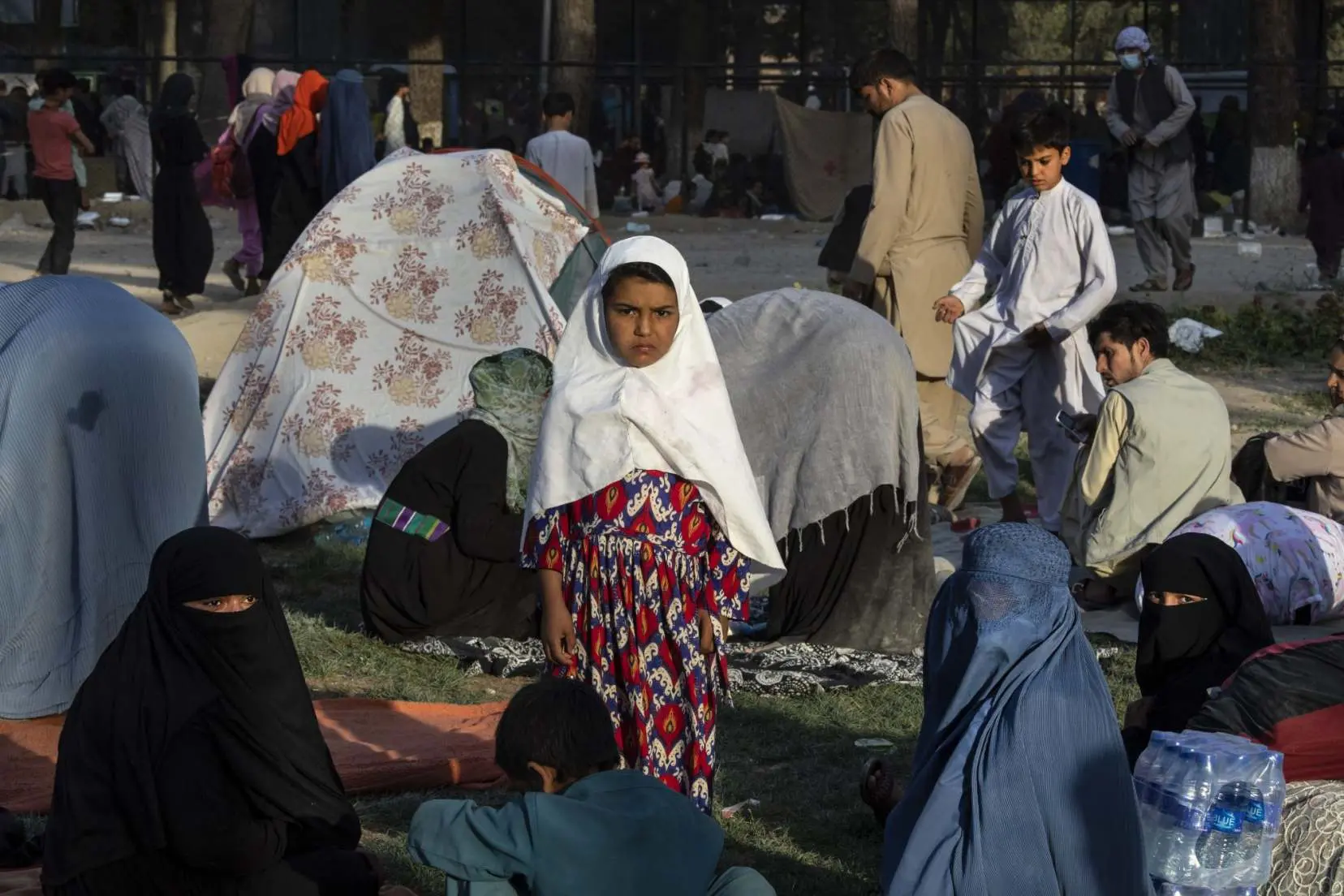 Girl stands amongst other displaced Afghans