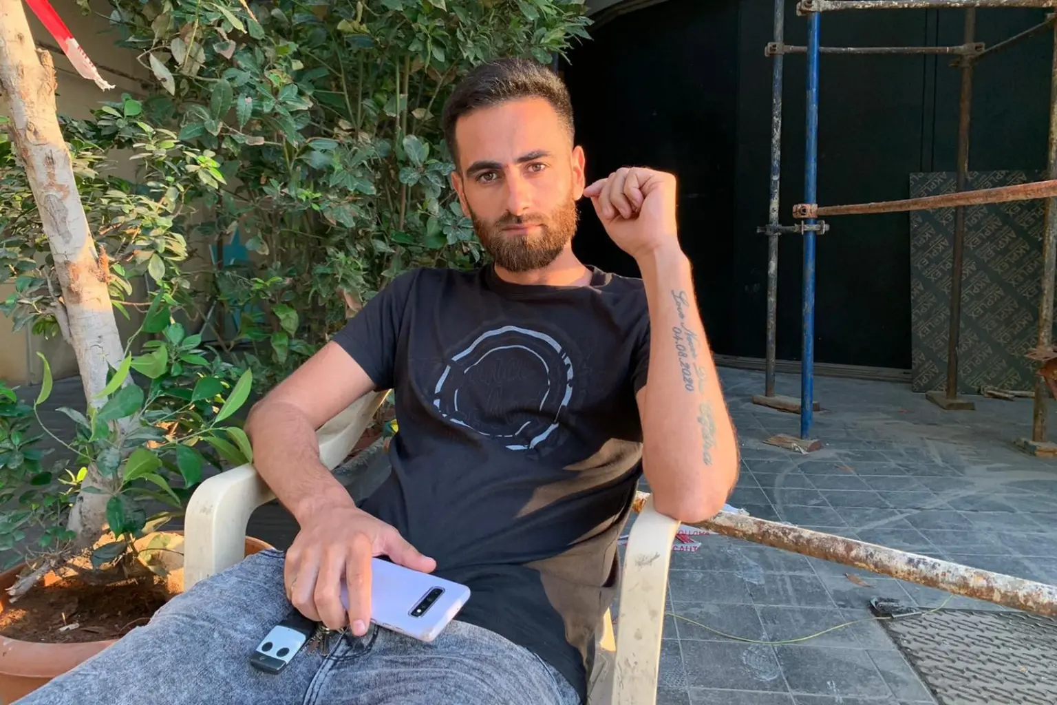 Mahmoud al-Kanu sits outside the largely vacant office building where he works as a guard near Beirut’s port on May 23. The tattoo on his left arm reads: “Love Never Dies, Cidra. August 4, 2020.”