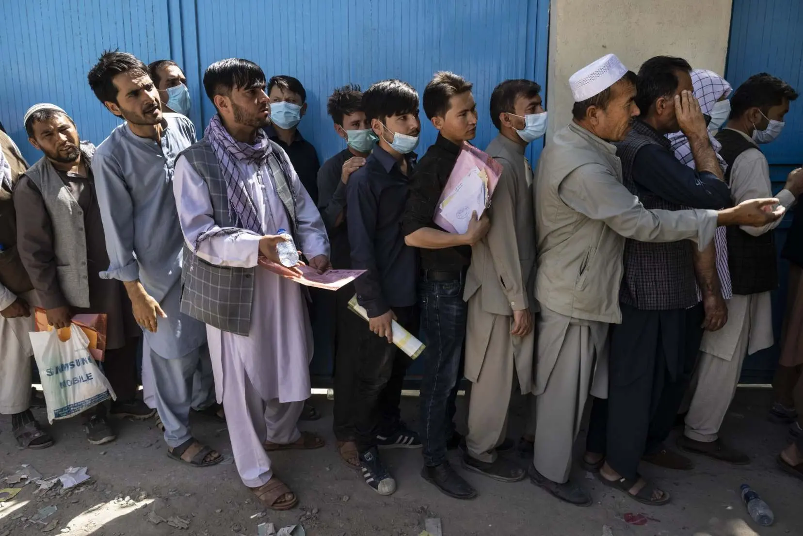 A line of men wait in line with visa documents