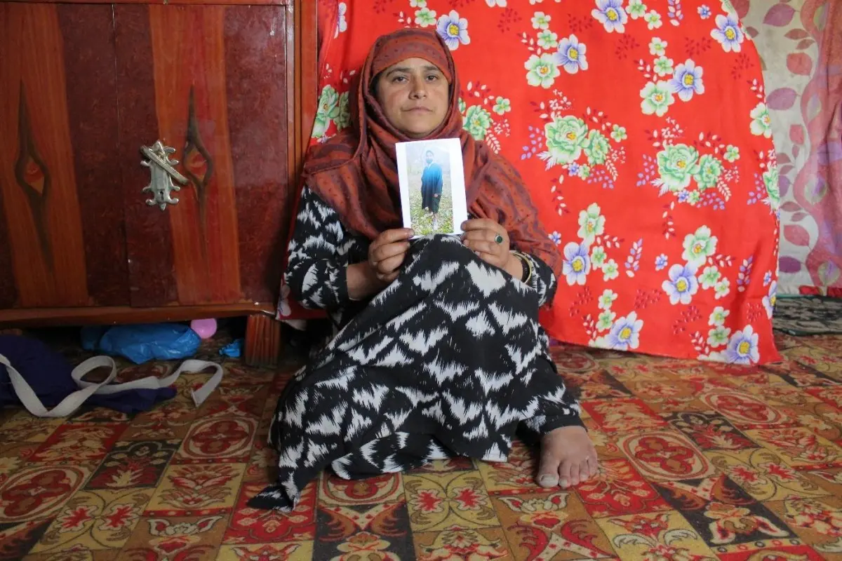 A mother holds a photo of her son in her home