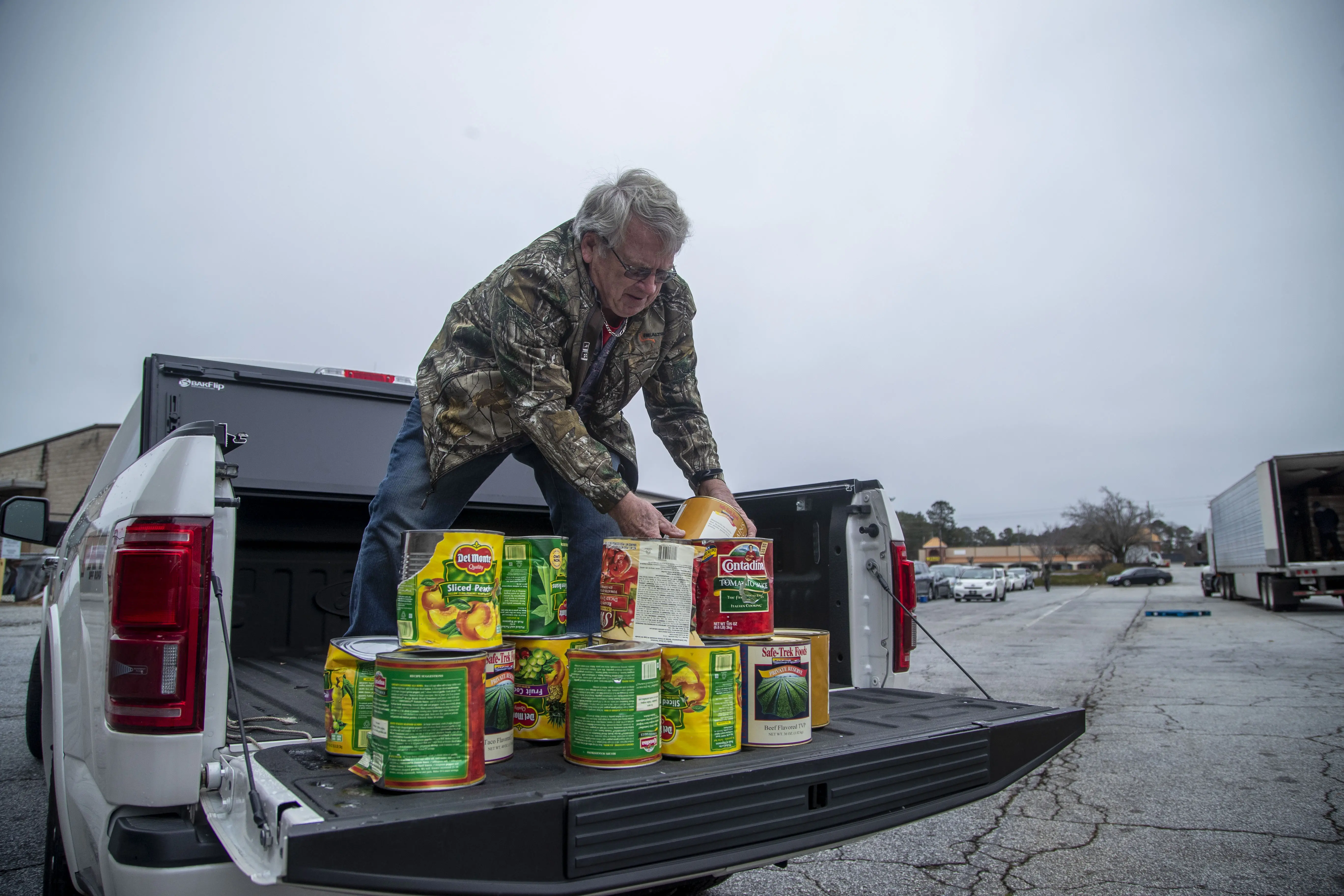 A man stacks large cans of food on a truck bed.